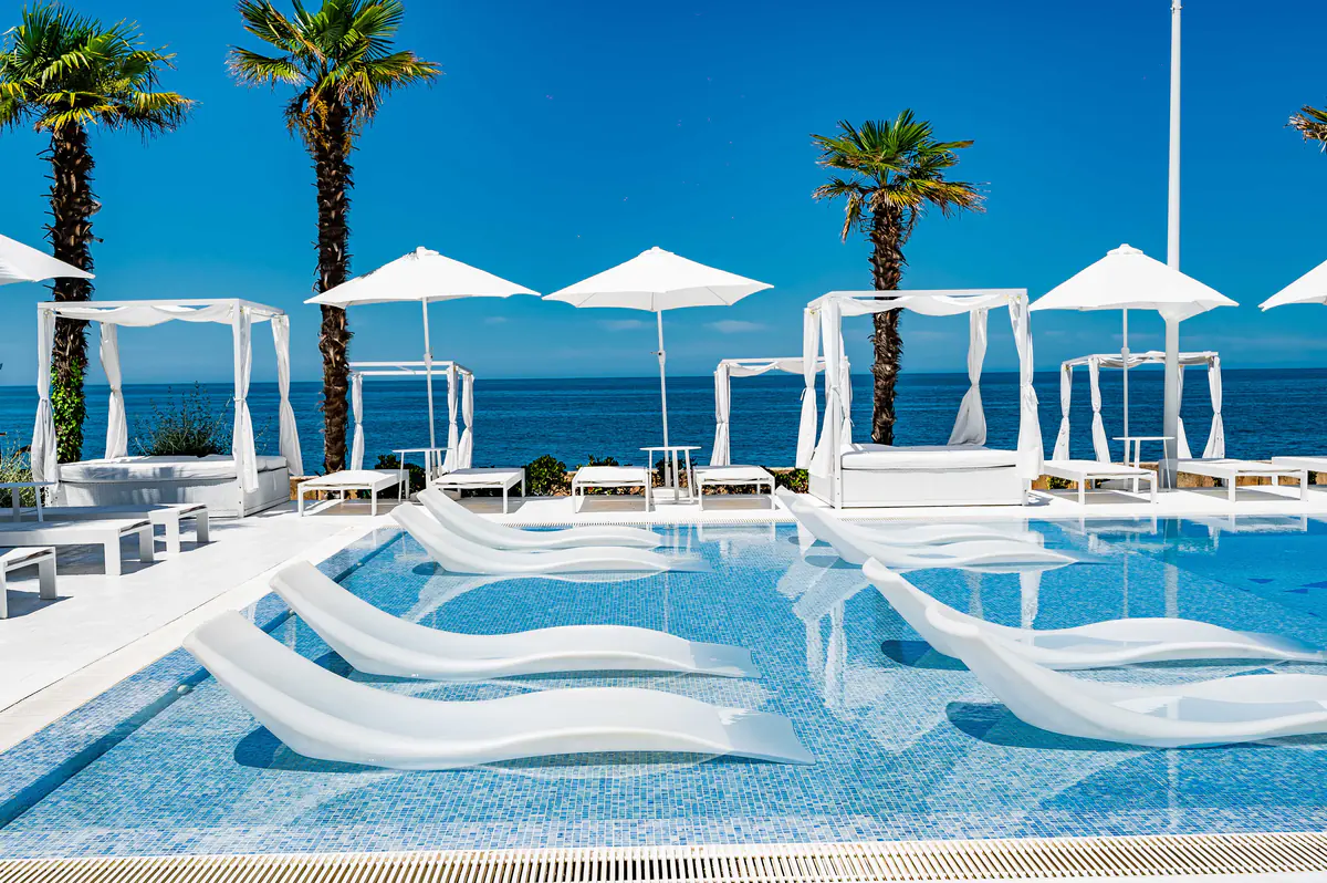 The beach club pool with cabanas and the sea behind it